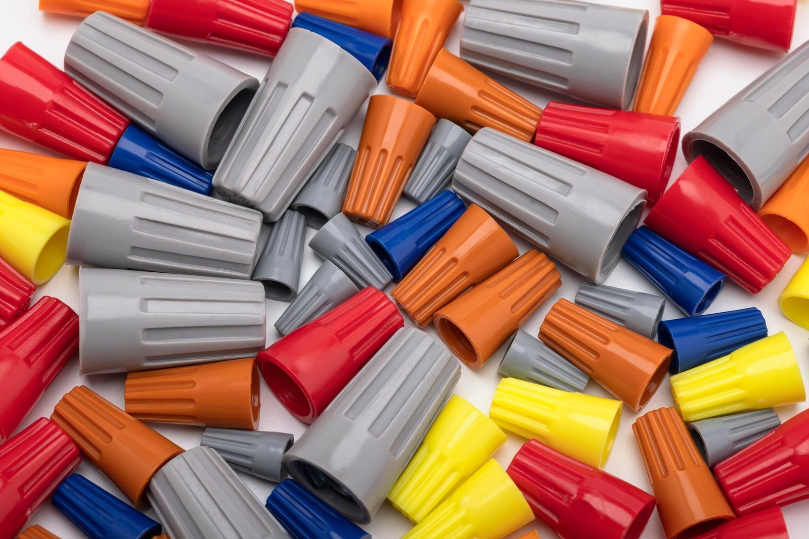 Colorful electrical wire connectors are scattered randomly on a white surface, showcasing a variety of shapes and sizes in red, blue, yellow