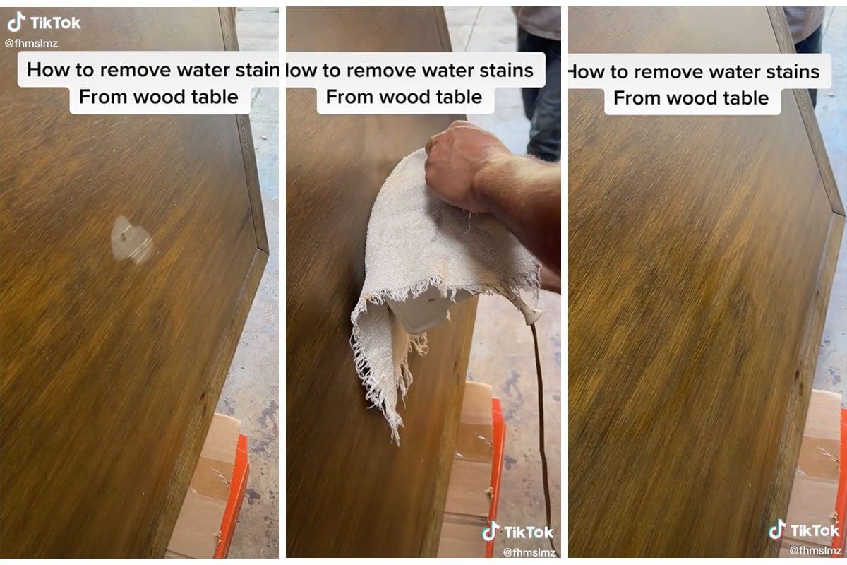 A person's hand wipes a wood table with a cloth, removing a water stain, while surrounded by a workshop environment with tools and cardboard