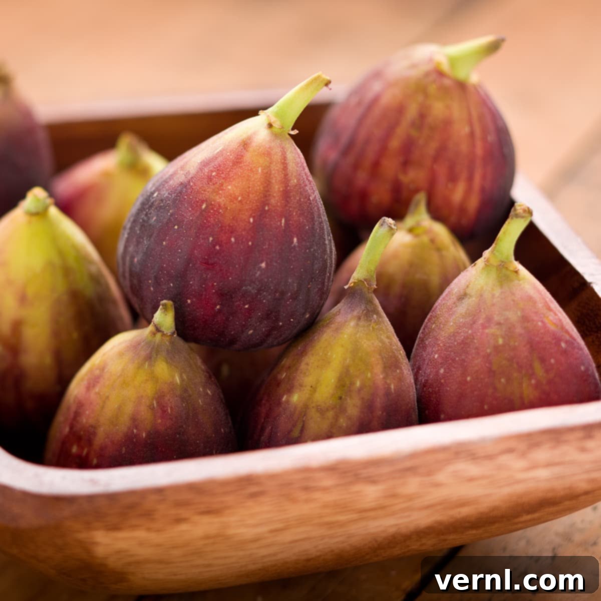 Figs in a Bowl-4636 Ένα καφέ ξύλινο μπολ με μαύρα σύκα mission με μοβ φλούδα και πράσινες κορυφές.