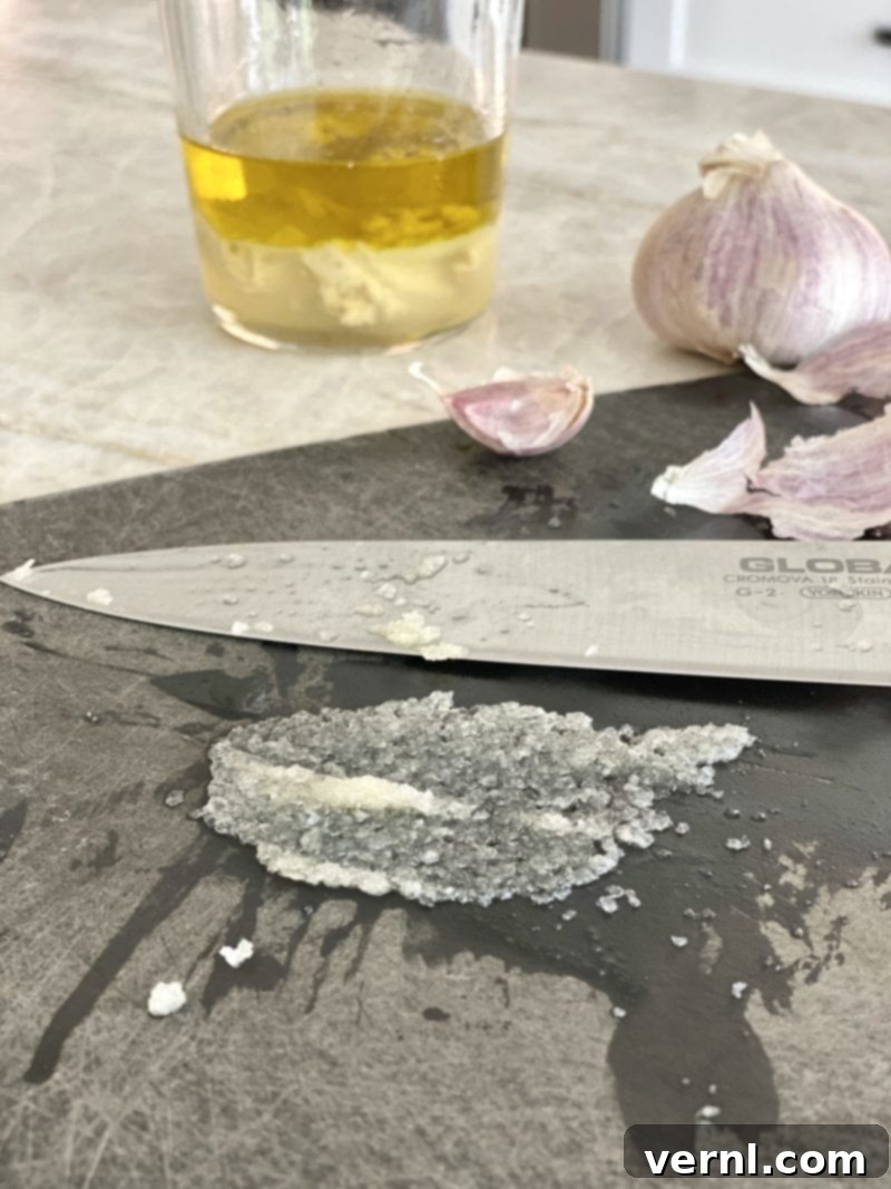 Κρεμώδης Σάλτσα Ταχινιού με Λεμόνι 3 Απλώνω ψιλοκομμένο σκόρδο σε μια πάστα σε ξύλο κοπής.