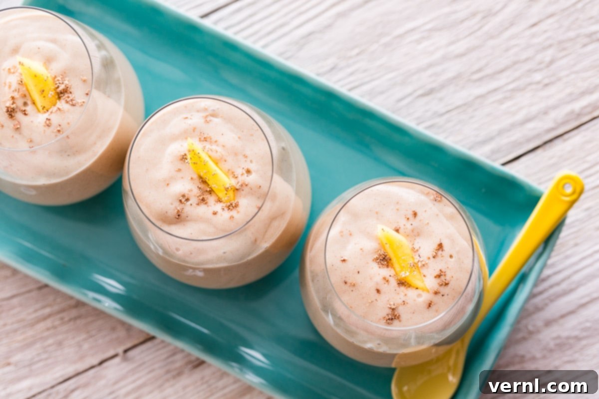 Κοντινό πλάνο ενός smoothie καρύδας-μάνγκο σε ένα ποτήρι γαρνιρισμένο με μάνγκο.