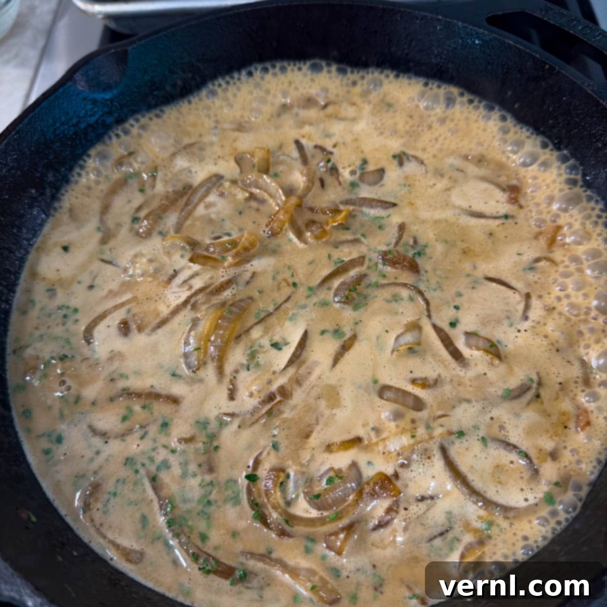 Χοιρινές Μπριζόλες Ξινής Κρέμας 11 A sour cream onion sauce cooking down on the stovetop in a cast iron pan.