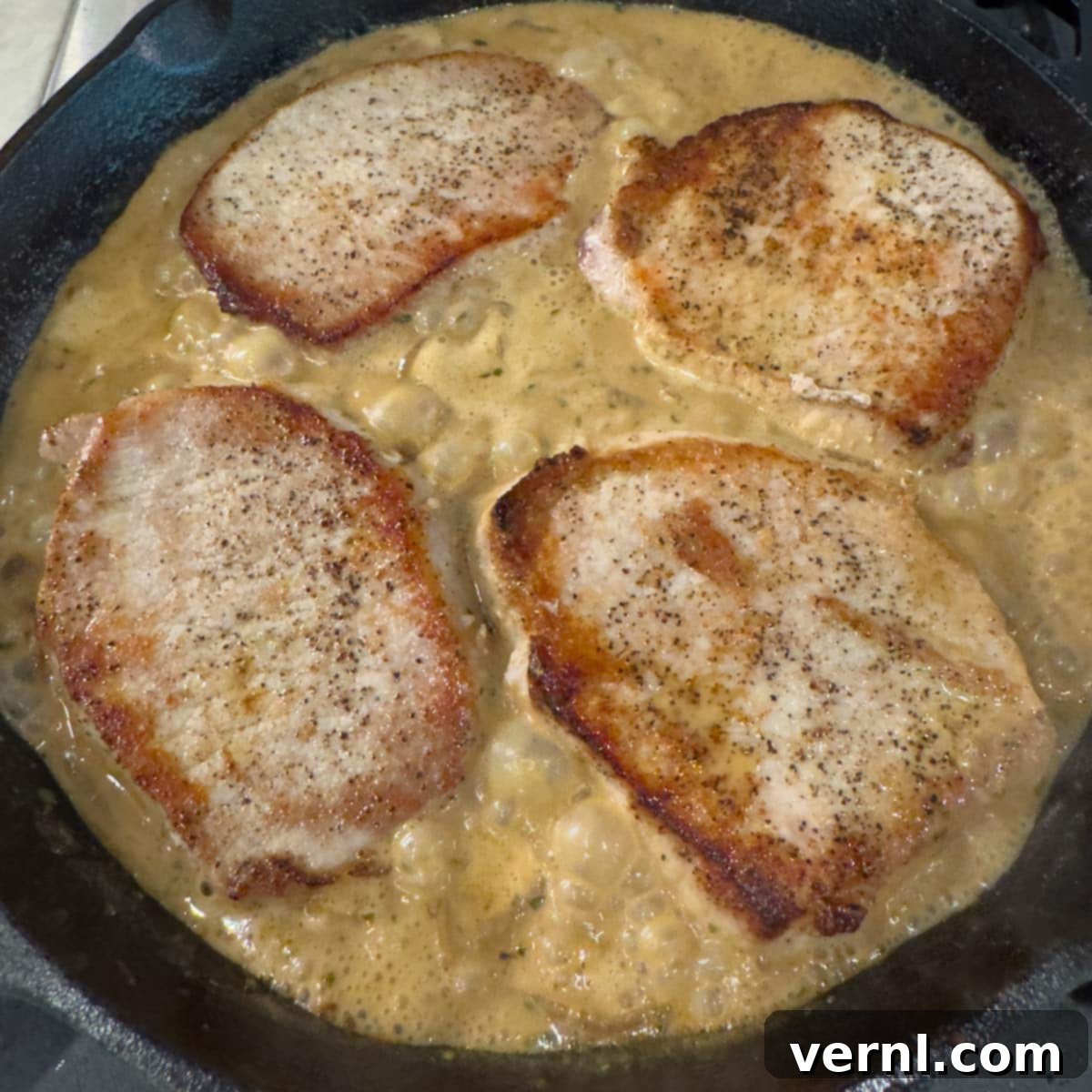 Χοιρινές Μπριζόλες Ξινής Κρέμας 12 Boneless pork chops in a black skillet on top of sauce to be cooked down.