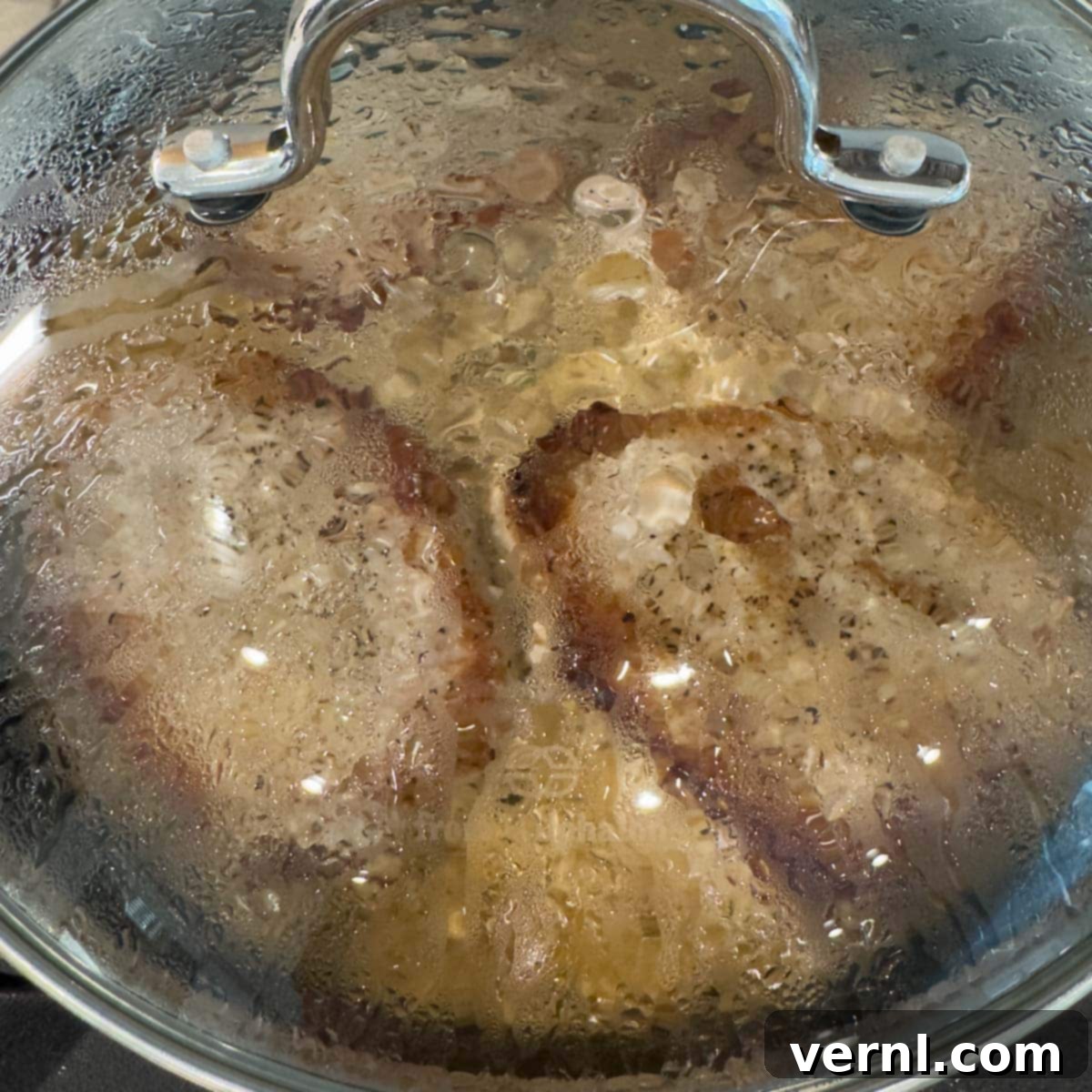 Χοιρινές Μπριζόλες Ξινής Κρέμας 13 Pork chops under a glass lid to finish cooking on the stovetop.