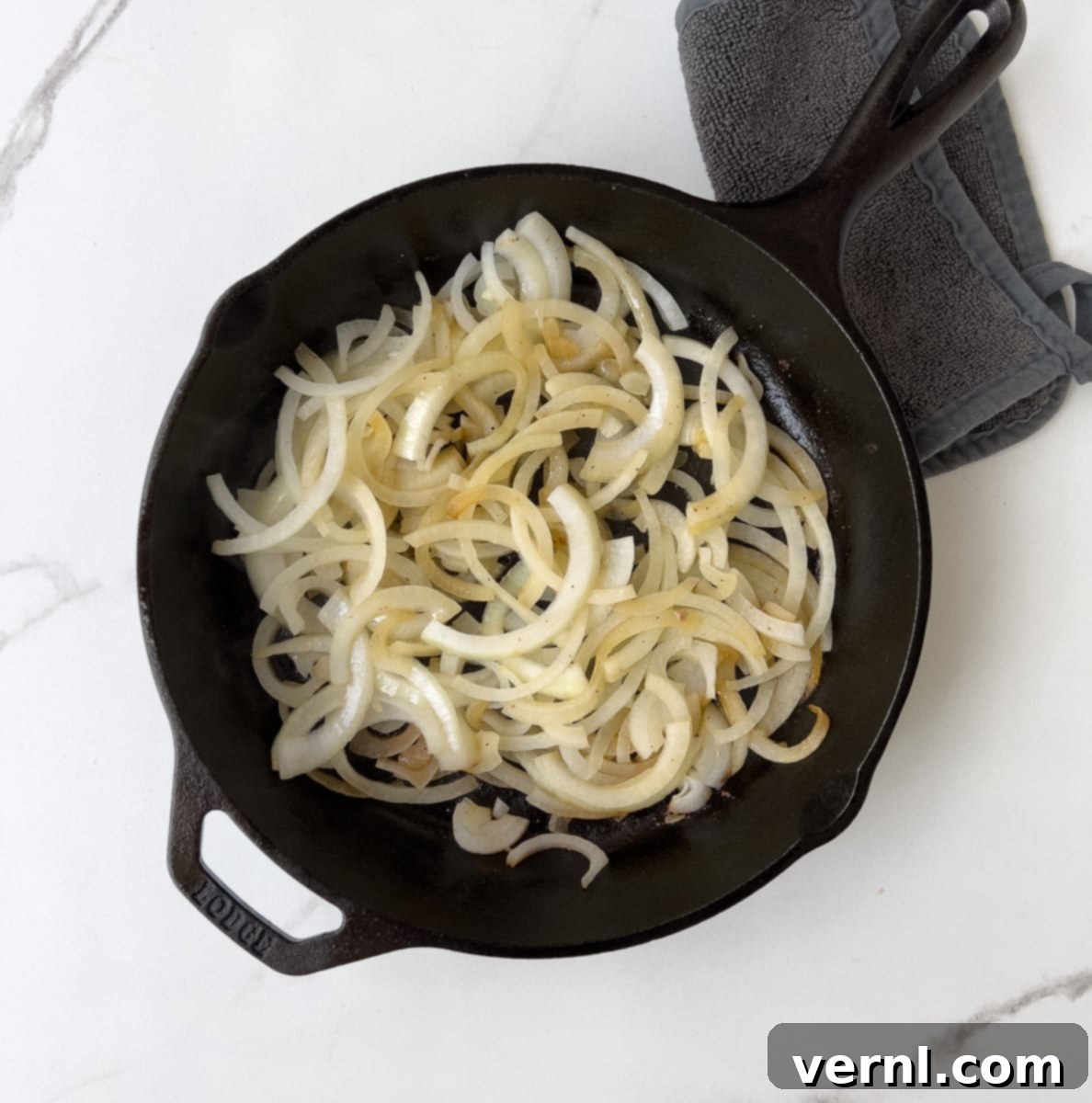 Χοιρινές Μπριζόλες Ξινής Κρέμας 6 Sliced onions cooking in a cast iron pan.