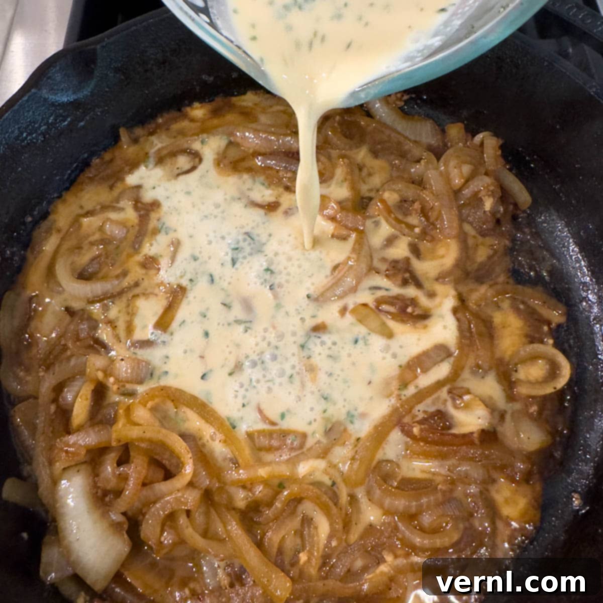 Χοιρινές Μπριζόλες Ξινής Κρέμας 10 Creamy sauce mixture pouring into a pan of caramelized onions to make a sauce.