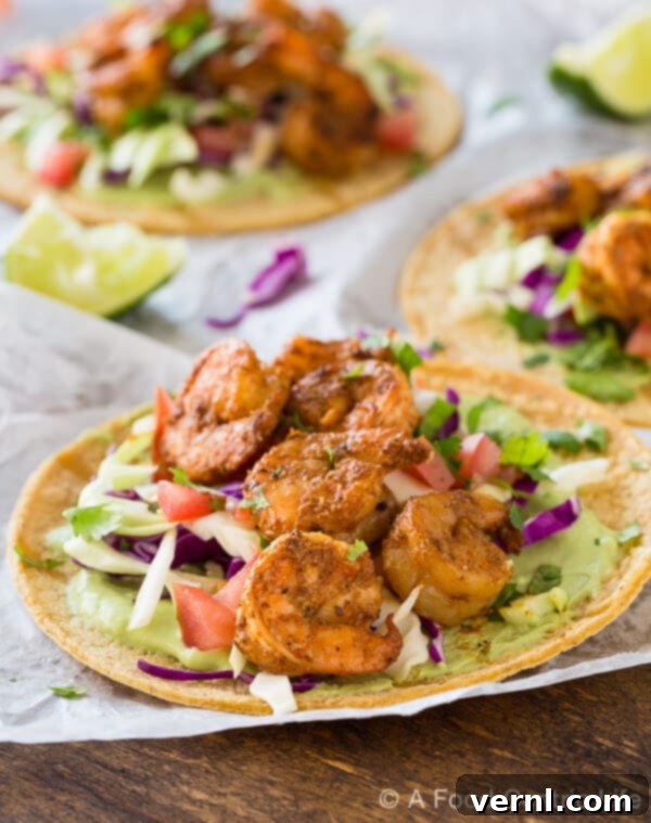 Ψητά tacos με γαρίδες στοιβαγμένα σε λευκό χαρτί πάνω σε ξύλινο τραπέζι, με σάλτσα αβοκάντο και λαχανικά.