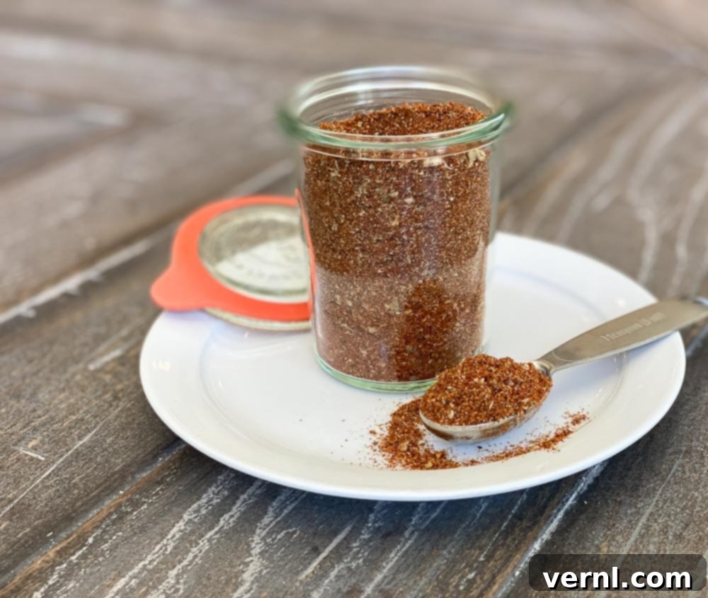 Σπιτικό μείγμα μπαχαρικών για tacos με σκούρο, σκουριασμένο χρώμα σε ένα βάζο, πάνω σε ένα λευκό πιάτο με ένα κουτάλι της σούπας.