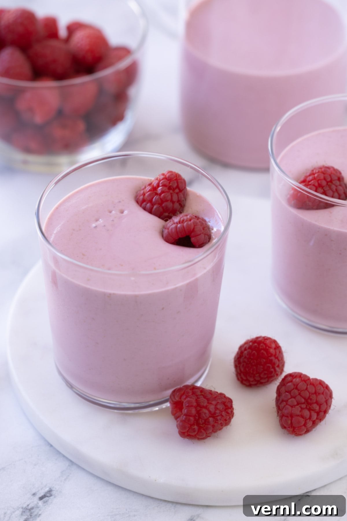 Σμούθι με Σμέουρα 2 Ένα όμορφο ροζ smoothie με σμέουρα σε ένα μικρό ποτήρι, με ένα μπολ γεμάτο σμέουρα στο πλάι.