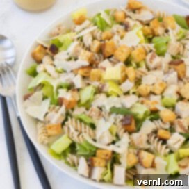 Σαλάτα Ζυμαρικών Καίσαρα με Κοτόπουλο 11 A Caesar pasta salad ready to serve with salad servers and dressing in a marble counter.