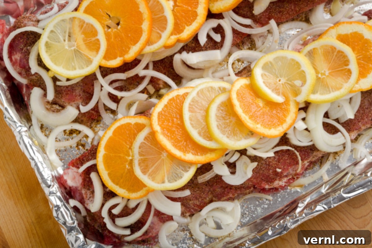 Μαλακά Χοιρινά Πλευράκια Φούρνου 3 Baby back ribs καλυμμένα με φέτες κρεμμυδιού, λεμονιού και πορτοκαλιού σε ταψί με αλουμινόχαρτο.