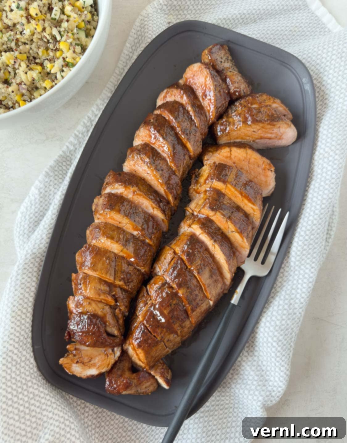 Καπνιστό χοιρινό ψαρονέφρι 2 Sliced pork tenderloins glazed with bbq sauce on a gray platter with a salad beside.