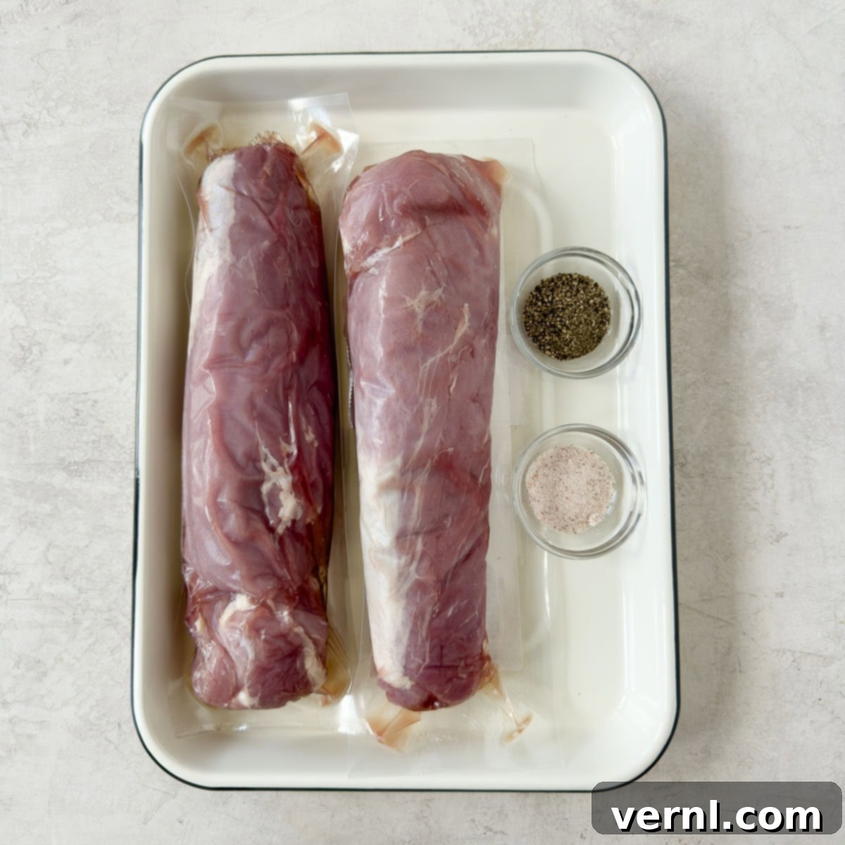 Καπνιστό χοιρινό ψαρονέφρι 3 Raw pink pork tenderloins on a white tray with small bowls of salt and pepper to season.