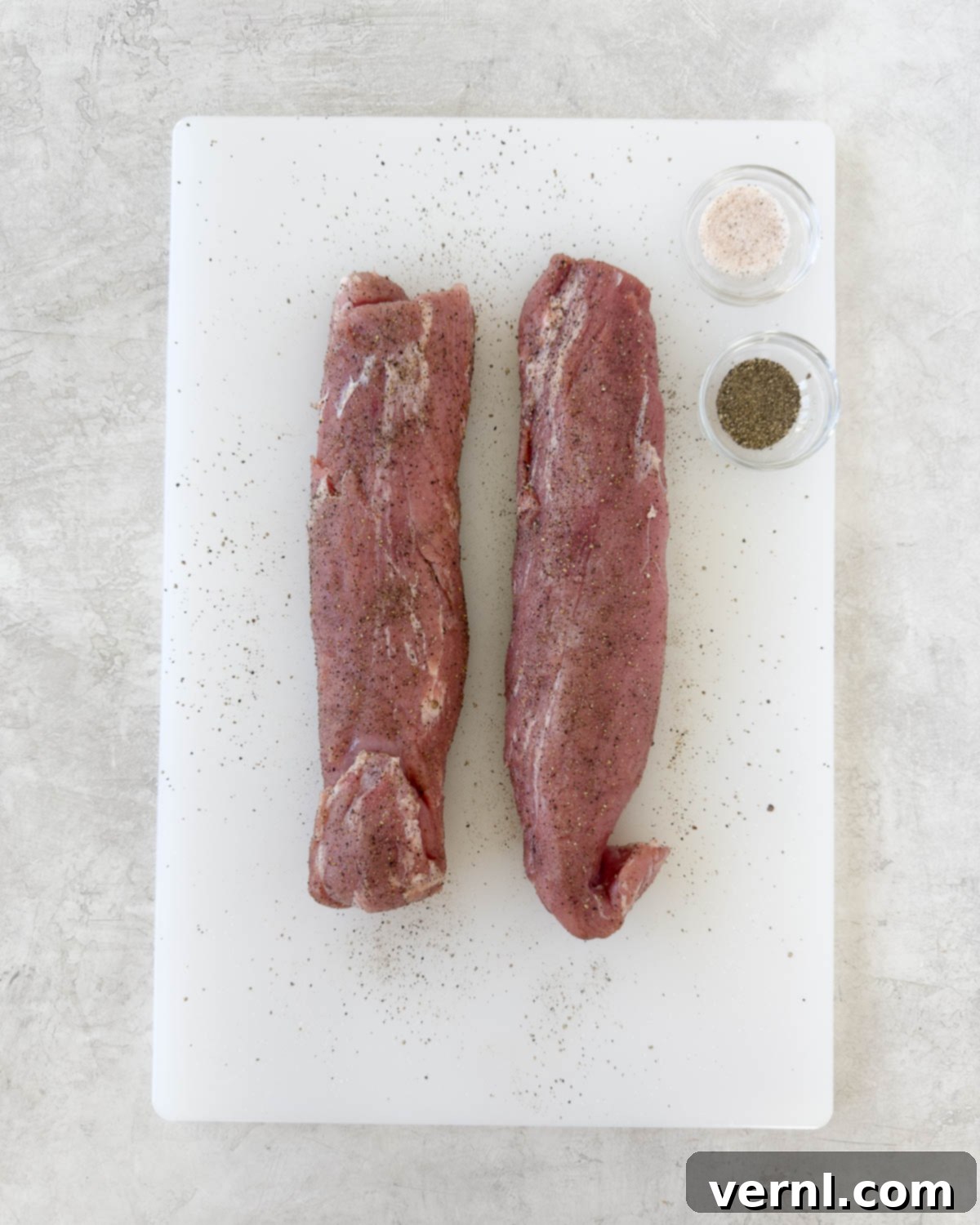 Καπνιστό χοιρινό ψαρονέφρι 5 Pork tenderloin being seasoned with salt and pepper on a white cutting board.