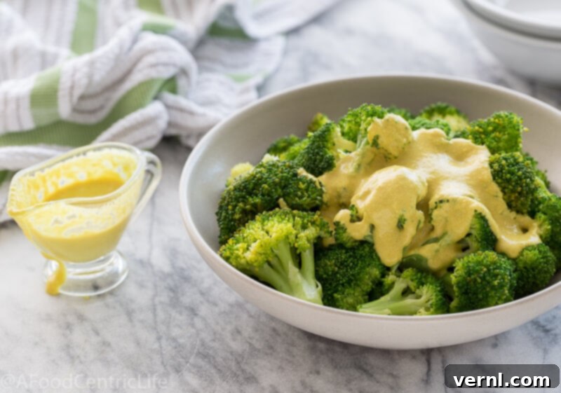 vegan cheese sauce | AFoodCentricLife.com Βίγκαν τυροσαλάτα πάνω από φωτεινό πράσινο μπρόκολο στον ατμό σε ένα μπολ.