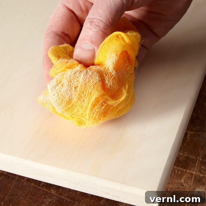 Tack Cloth The Unsung Hero of DIY Finishes 2 A person gently wiping a wooden surface with a yellow tack cloth, demonstrating proper dust removal before finishing.