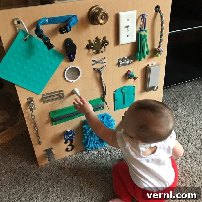 Craft a Toddler Busy Board from Everyday Essentials 2 A smiling baby with bright eyes reaches out to interact with a colorful busy board, showcasing the pure joy and engagement this sensory toy brings to early childhood development.