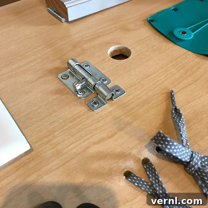 Craft a Toddler Busy Board from Everyday Essentials 5 Close-up view of a hand carefully screwing a latch onto a wooden busy board, demonstrating the secure attachment process for toddler activity items.