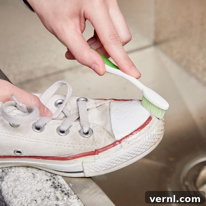 Toothpaste Sneaker Cleaning Hack 2 A person cleaning white sneakers with a toothbrush and white toothpaste, highlighting the cleaning process for sparkling shoes.