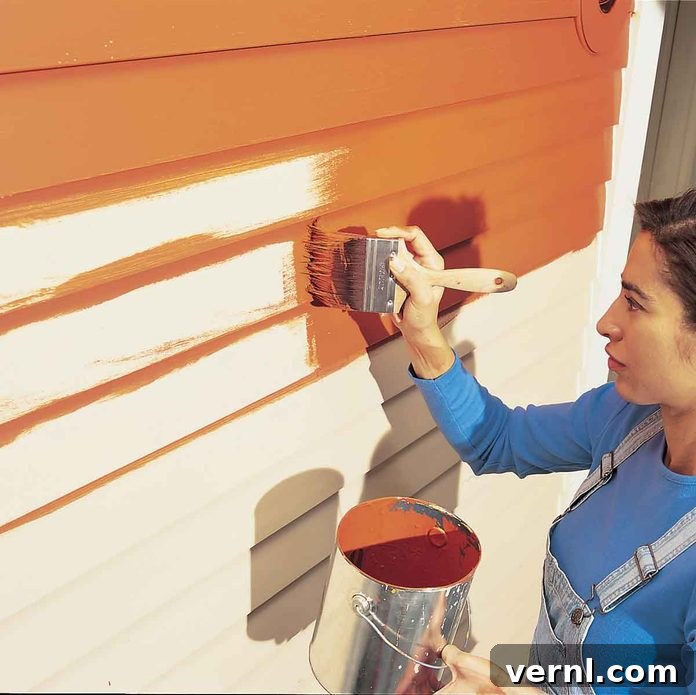 Elevate Your Home: The Ultimate Guide to Choosing Paint Colors Now 3 Woman painting a house with a roller, adding a coat of red-orange paint, illustrating home renovation.