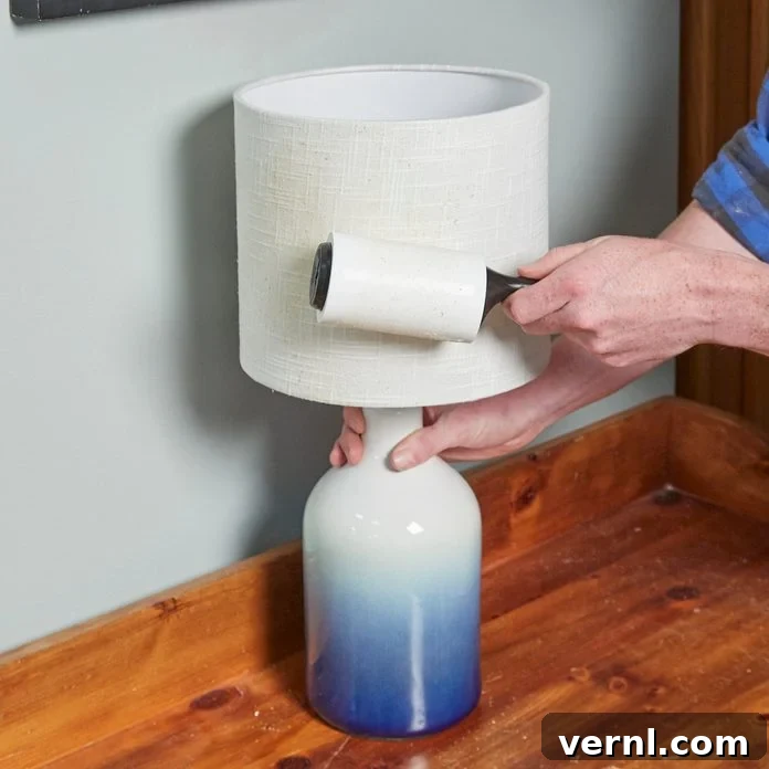 Lampshade Revival: Illuminating Your Home Again 3 Person gently cleaning a lampshade with a lint roller to remove dust and pet hair