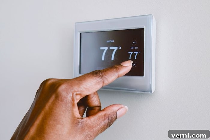 Smart Energy Moves: Cut Costs, Boost Efficiency 3 A hand is adjusting a digital thermostat, setting the indoor temperature to 77°F, mounted on a plain wall in a well-lit room.
