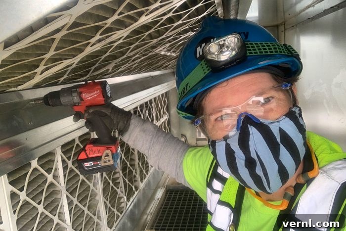 Soph Davenberry, a nonbinary sheet metal worker, holds a drill and wears a hard hat while working on a construction site, embodying the spirit of women and nonbinary tradespeople in the industry.