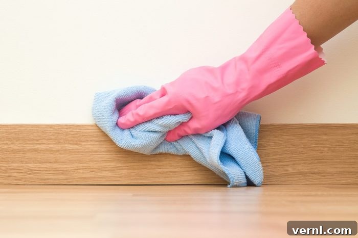 Mastering Dust Removal for a Spotless Home 2 Employee hand in rubber protective glove with micro fiber cloth wiping a baseboard on the floor from dust at the wall. Spring general or regular clean up. Commercial cleaning company concept.