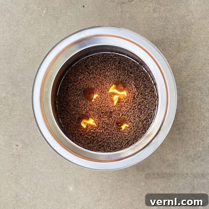Solo Stove Pellet Adapter: Tested, Reviewed, and Revealed 4 A metal container filled with small brown pellets has flames emerging from some, resting on a flat, light-colored surface.