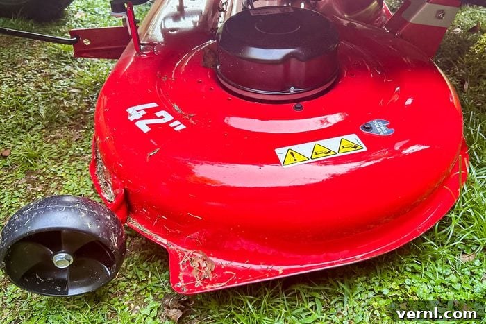 Craftsman's Electric Rider: Taming Tight Spaces with Ease 3 A red mower deck rests on green grass, displaying a 42-inch label, with a black wheel and warning symbols for safety.