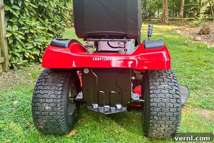 Craftsman's Electric Rider: Taming Tight Spaces with Ease 4 A red lawn mower stands on green grass, with the rear view showing large wheels, a seat, and garden foliage in the background.