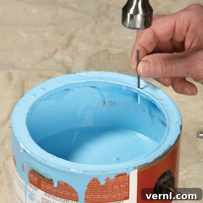 Hammering a small nail into the side of a paint can rim to drain excess paint back into the can, a crucial step for superior paint storage and preservation.