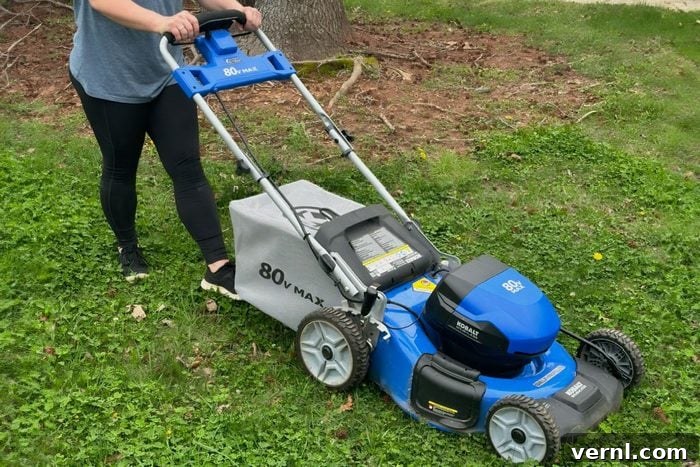 A woman efficiently using a Kobalt electric mower to cut grass in her front yard, demonstrating ease of use.