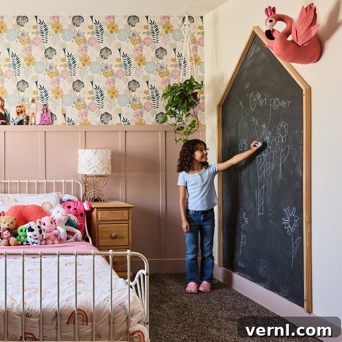 The Craft of Influence: Kyle Ortiz's DIY Legacy Home 5 A young child stands at a large chalkboard shaped like a house, drawing with chalk in a child's bedroom. The room features floral wallpaper, a bed with stuffed animals, a nightstand with a lamp, and a flamingo wall decoration.