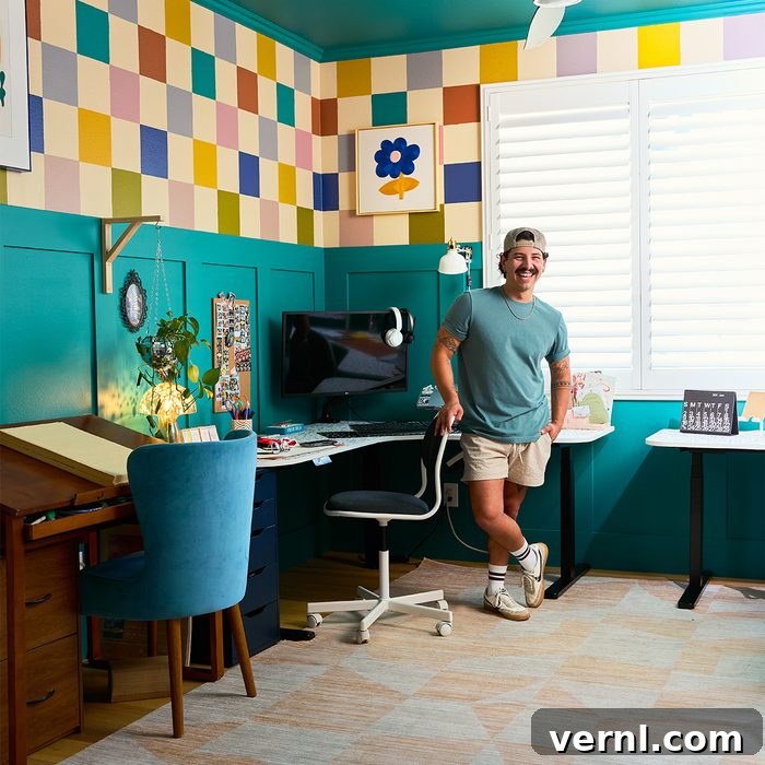 The Craft of Influence: Kyle Ortiz's DIY Legacy Home 7 A person stands in a colorful, well-organized room featuring teal walls and a checkerboard pattern above. The room includes a desk with a computer, a drafting table, a chair with plush blue cushion, and various decorative elements, including a plant and artwork.