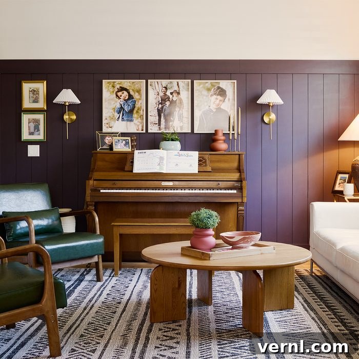 The Craft of Influence: Kyle Ortiz's DIY Legacy Home 8 A cozy living room with a wood-paneled wall features a piano with sheet music, family photos, and sconces above. Green and white armchairs sit around a round wooden coffee table on a patterned rug. A table lamp and decorative items add a warm ambiance.