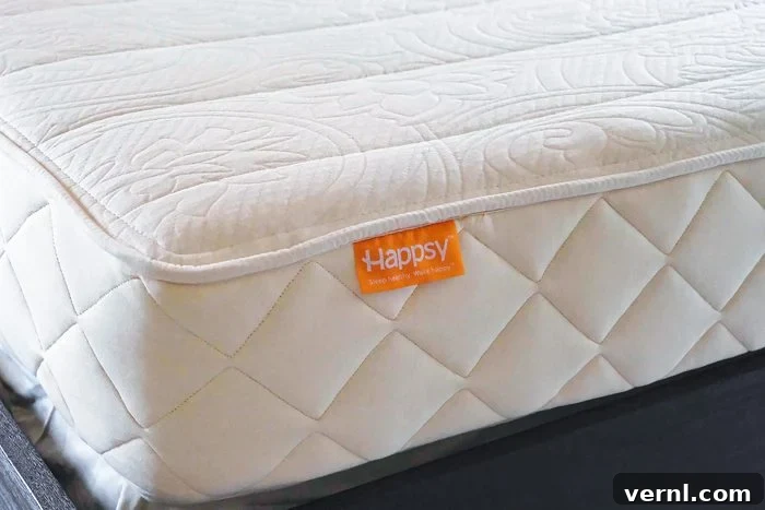 Happsy Mattress Review Organic Comfort for Allergy Sufferers 4 Detailed close-up of a cream-colored, quilted Happsy organic mattress. The distinctive orange Happsy label is clearly visible on the side, and the mattress surface features an elegant, textured circular pattern, all resting securely on a dark base.