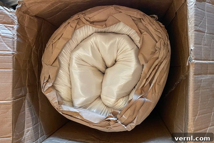 Happsy Mattress Review Organic Comfort for Allergy Sufferers 5 A securely rolled-up mattress, neatly encased in white fabric and brown paper, is positioned inside a sturdy cardboard box, ready for unboxing.