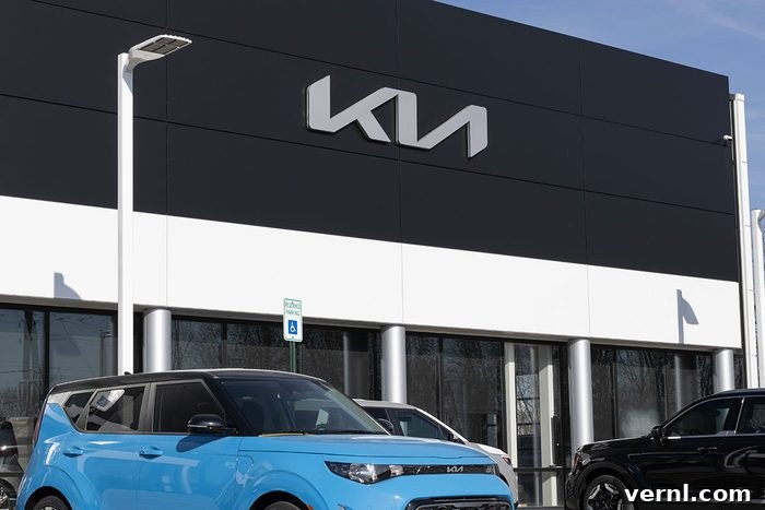 The KN Car Logo: Debunking the Viral New Brand Myth 2 A modern Kia dealership storefront featuring the new stylized Kia logo prominently displayed. The building has large glass windows, reflecting a bright, clean environment, with several new Kia vehicles visible inside and outside, all bearing the updated emblem.