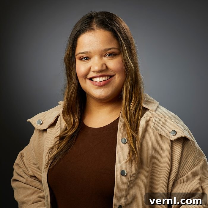 Family Handyman's Women Share Their DIY Insights 4 A woman with long wavy hair smiles at the camera. She is wearing a brown top and a light beige corduroy jacket, standing against a dark, plain background. Her expression is pleasant and thoughtful.
