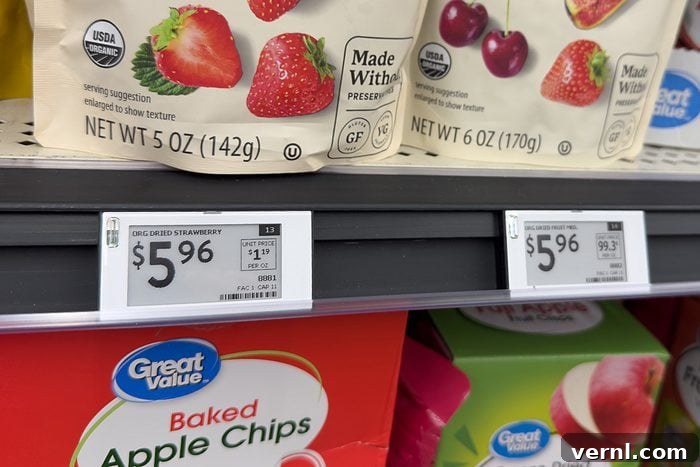 Close-up of store shelves displaying snack packages, including dried strawberries and cherries above, each priced at $5.96, and boxes of Great Value Baked Apple Chips below. Digital price tags are visible.