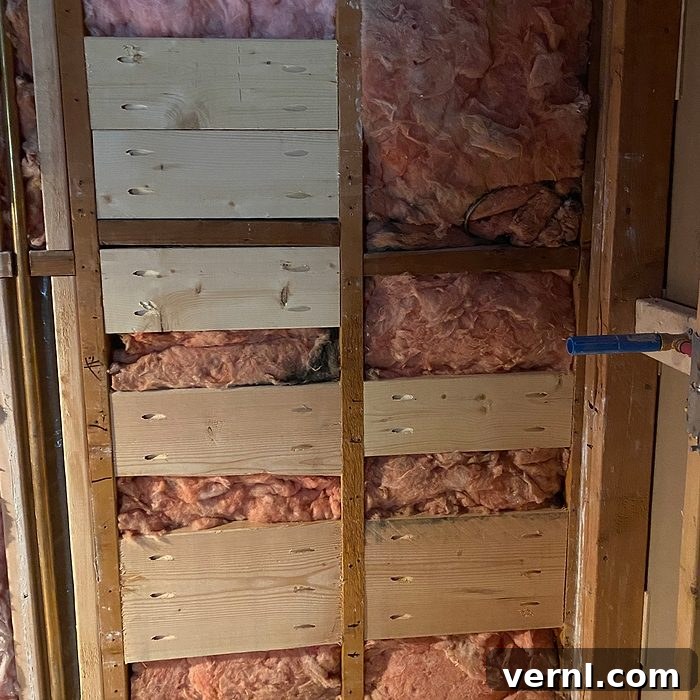 Why I Stopped Renovating for Style and Focused on Function 3 Wooden wall framing with insulation material in pink, showing horizontal wooden boards and a blue pipe.