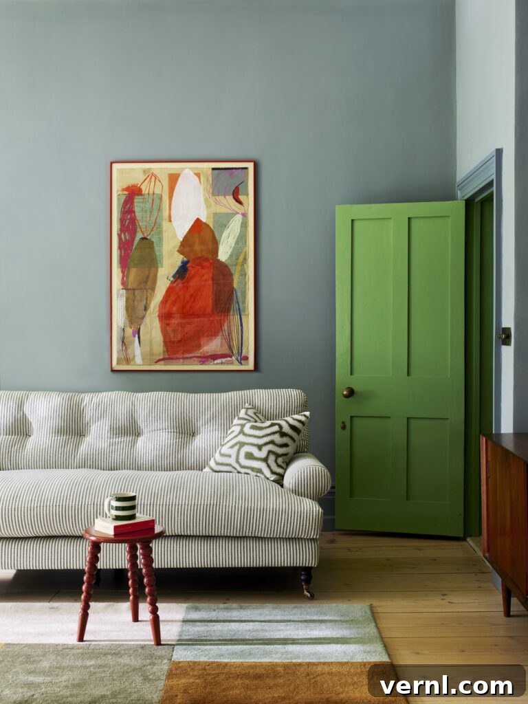 Blue living room with a striped sofa, bold green door, abstract wall art, and small red accent table.