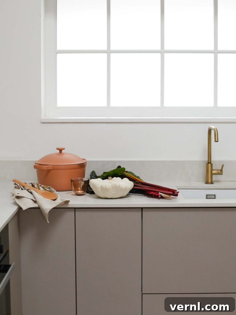 Minimalist kitchen with neutral cabinets, brass faucet, and blush cookware with white pumpkin on the counter.