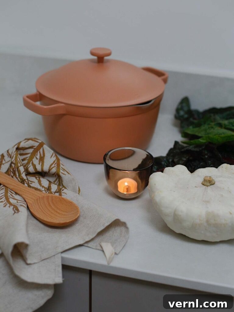 Earthy kitchen decor with a pink Our Place Perfect Pot, candlelight, white pumpkin, and fall vegetables on the countertop.