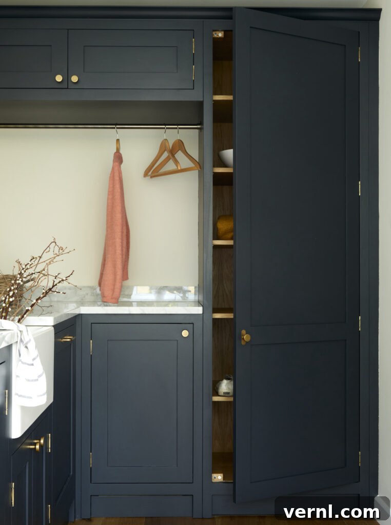 Why Homeowners Move Laundry Rooms Upstairs — And You Should Too 5 Laundry room upstairs featuring navy cabinetry with brass accents, open shelving for storage, a hanging rail for clothes, and a marble countertop for folding and organisation.
