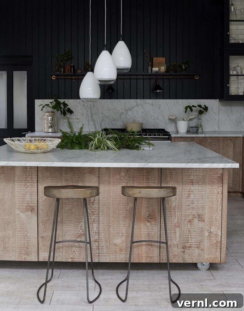 A light wood kitchen island on wheels with glass pendant lighting hanging above in a black painted kitchen.