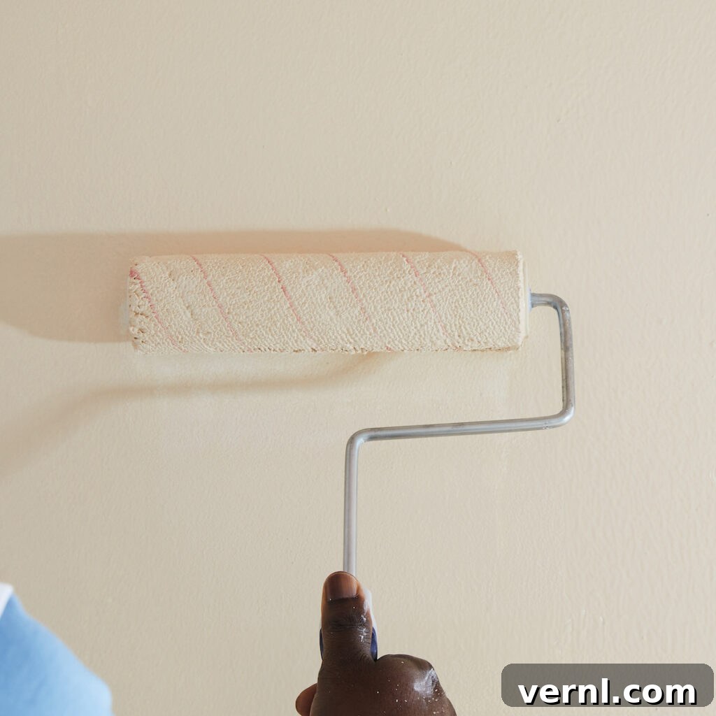 6 Colors That Complement Magnolia Walls for a Timeless Look 2 A hand holding a paint roller applying magnolia-colored paint to a wall.