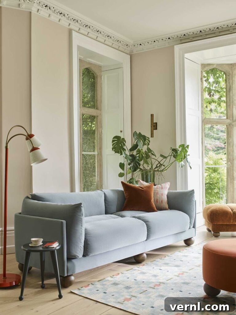 6 Colors That Complement Magnolia Walls for a Timeless Look 7 A cosy living room with magnolia walls, a soft blue sofa, and warm-toned pillows, featuring large windows with natural light and a mix of modern and vintage decor.