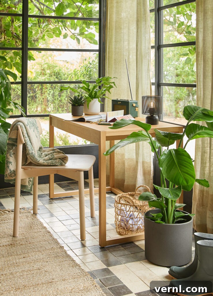 Refresh a Room That Feels Off Using Only Items You Already Own 6 Cosy home office with a wooden desk, potted plants, and natural light streaming through large windows with green curtains. A beige chair with a patterned throw blanket sits next to the desk, which holds an open book, a lamp, and a vintage radio. A woven basket and green rubber boots rest on the tiled floor.
